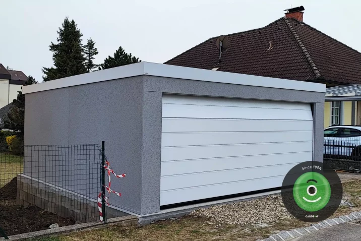 Garage mit grauem Putz und breitem weißen Tor