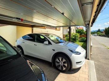 Zwei Autos sicher unter einem Carport mit braunem Garagentor geparkt.