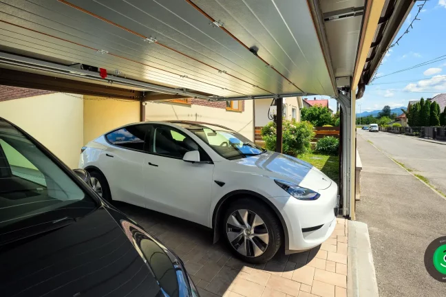 Zwei Autos sicher unter einem Carport mit braunem Garagentor geparkt.