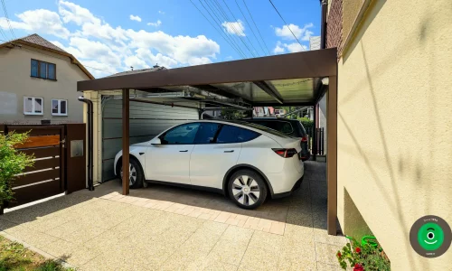 Autos geschützt unter einem Carport mit geschlossenem breitem Garagentor.
