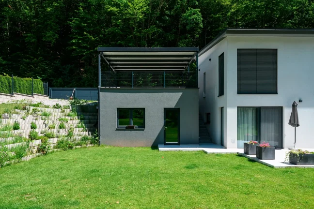Anthrazitfarbene Pergola mit Pultdach auf erhöhtem Untergrund montiert.