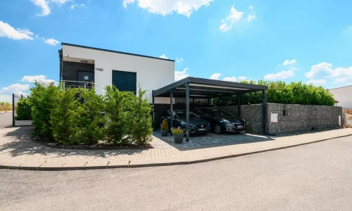 Anthrazitfarbenes Flachdach-Carport für zwei Fahrzeuge am Einfamilienhaus.