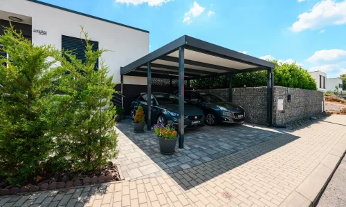 Zwei Fahrzeuge unter anthrazitfarbenem Stahl-Flachdach-Carport am Wohnhaus.
