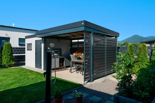 Anthrazitfarbenes Gartenhaus mit offenem Vordach und Metallfüllung der Wände.