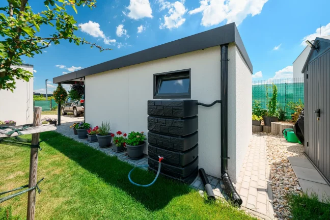 Regenwasserauffangbehälter am weißen Gartenhaus.