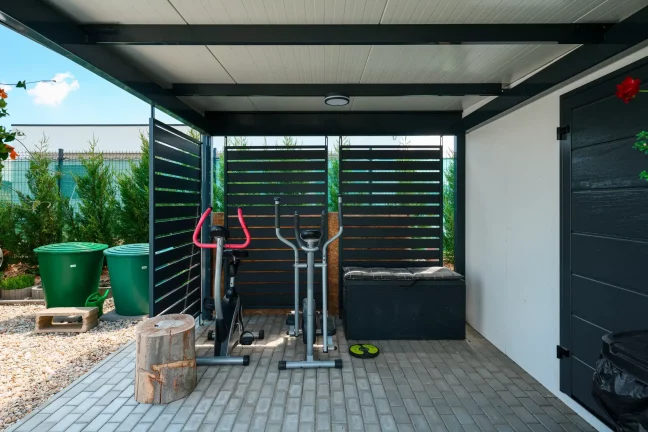 Fitnessbereich unter anthrazitfarbenem Carport mit Metall-Lamellen-Seitenwänden.