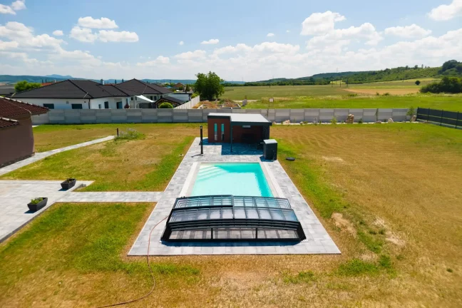 Gartenhaus mit dunklem Putz neben dem abgedeckten Schwimmbecken.