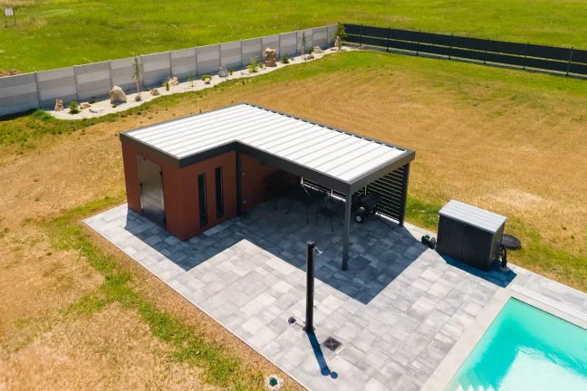 Ziegelbraunes Gartenhaus mit Carport am Pool.