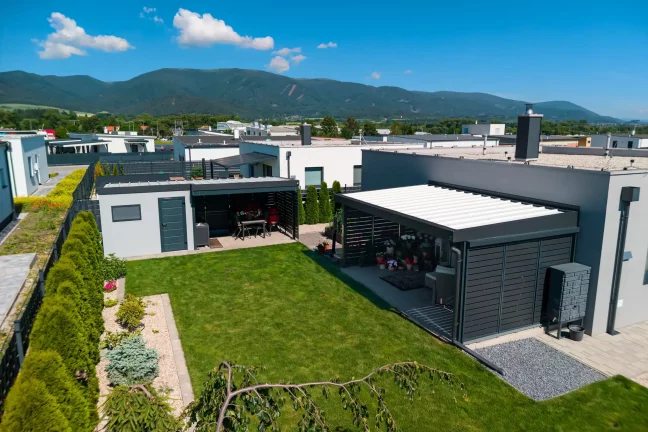 Anthrazitfarbenes Gartenhaus mit Pergola und Vordach mit Metallfüllung im Garten.