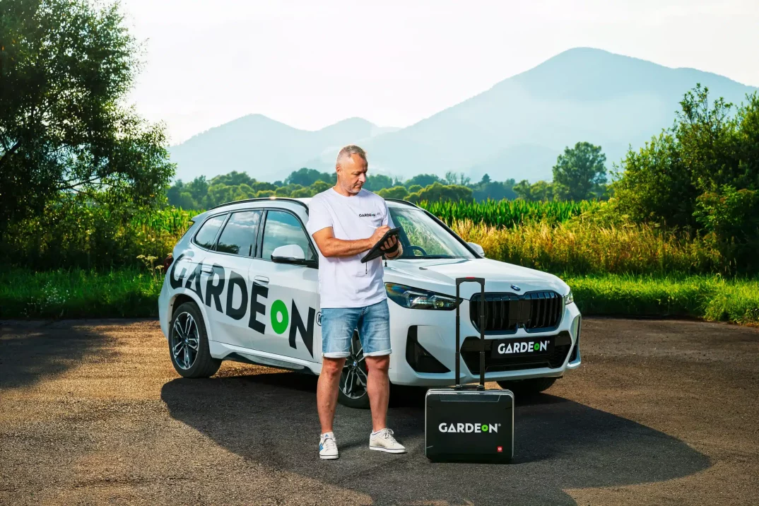 GARDEON-Agent mit Tablet, Firmen-BMW und Koffer in der Natur.