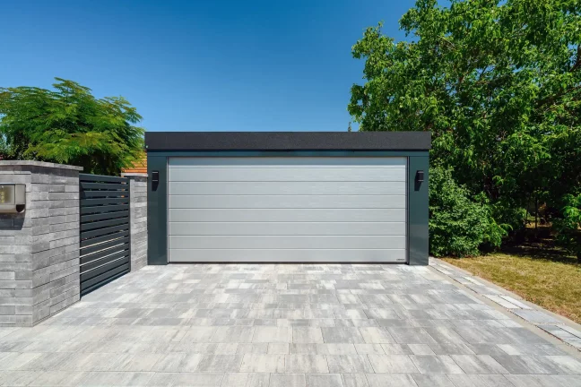 Geschlossenes silbernes Garagentor am Carport zwischen Bäumen