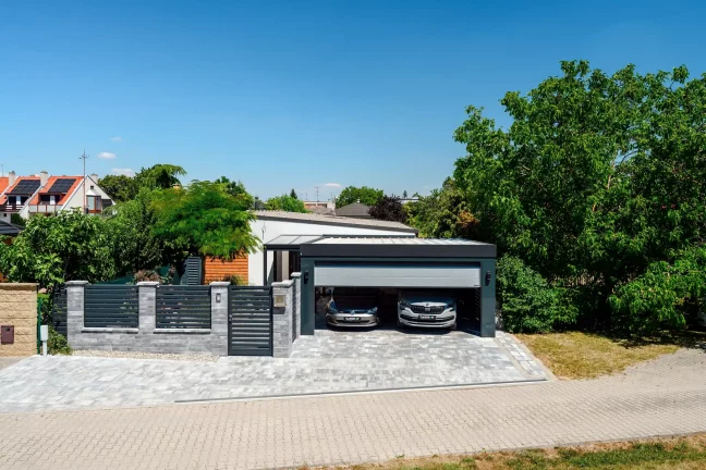 Haus mit Carport und zwei geparkten Autos am Zaun