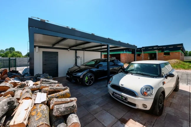 Blick vom Carport aus auf zwei Autos und ein Baugrundstück