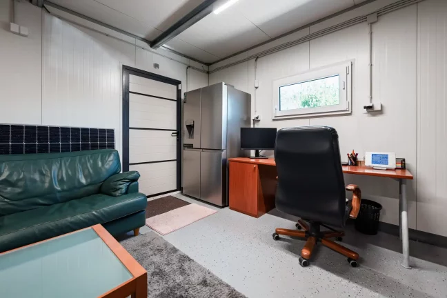 Raum mit grünem Sofa, Kühlschrank und Schreibtisch mit Monitor