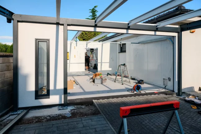 Blick in die im Bau befindliche Garage mit Stahlträgern für das Dach und einer Leiter