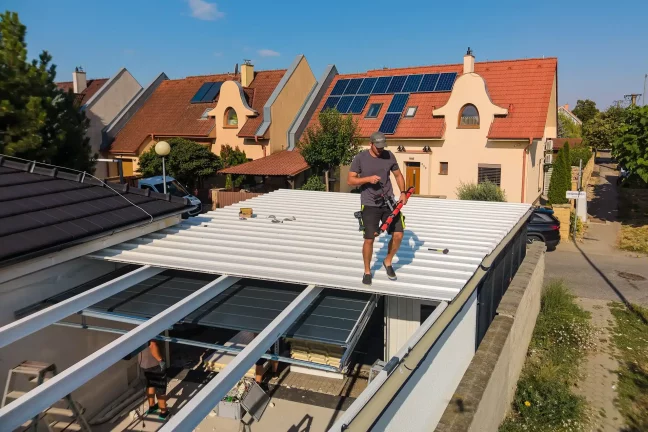 Luftaufnahme eines Monteurs auf dem Dach der Überdachung mit Messwerkzeug in der Hand