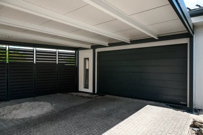 Fertige Garage mit dunklem Tor und Holzsichtschutz unter der Überdachung