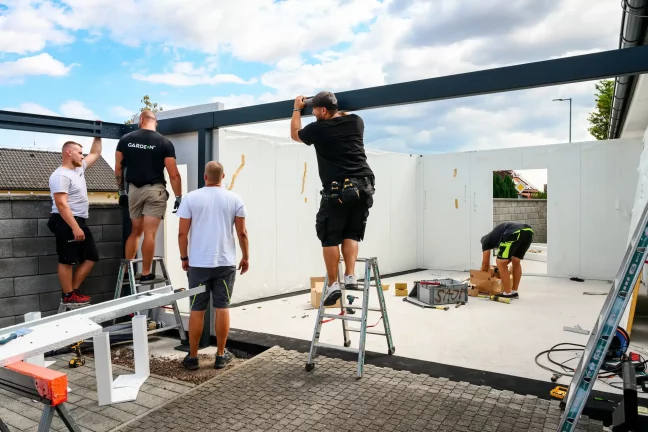 Monteure bringen mithilfe von Leitern weiße Wandpaneele an der Stahlkonstruktion der Garage an