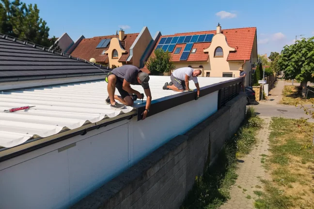 Zwei Mitarbeiter knien auf dem Dach der Überdachung und befestigen die Abschlussleiste