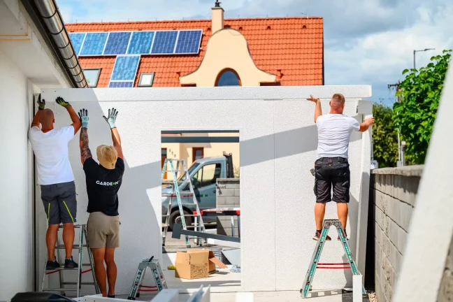 Drei Monteure auf Leitern montieren die obere Leiste der weißen Garagenwand
