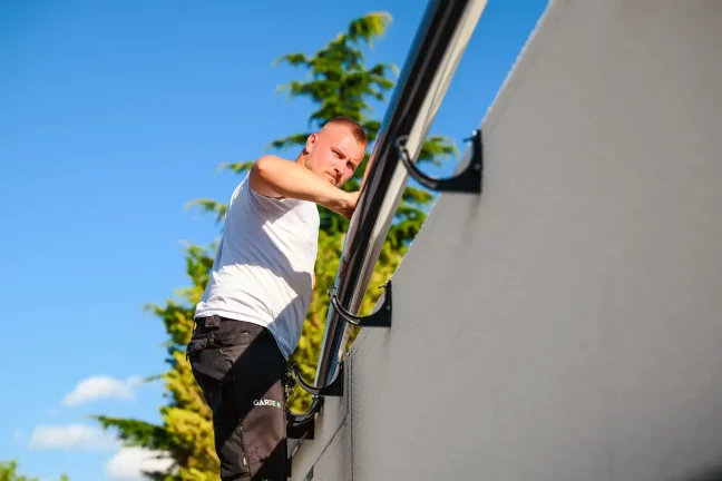 Mitarbeiter montiert ein Metallfallrohr an der grauen Garagenwand