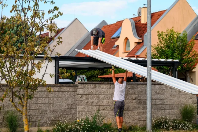 Mitarbeiter reicht einem Kollegen auf dem Dach ein weißes Dachpaneel