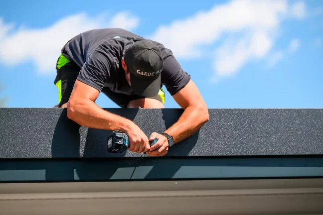 Detailaufnahme der Montage des dunklen Dachrinnensystems an der Garage