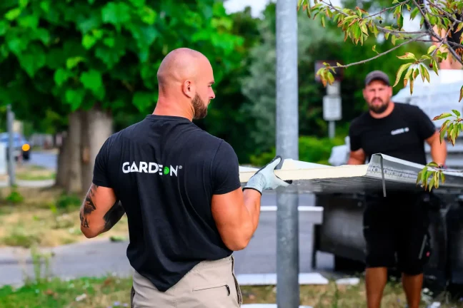 Zwei GARDEON-Mitarbeiter tragen gemeinsam ein Wandpaneel entlang der Straße