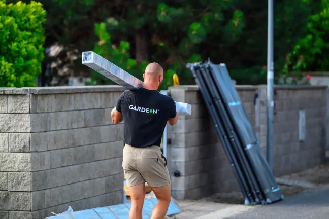 Mitarbeiter trägt verpackte Stahlträger auf der Schulter entlang der Mauer