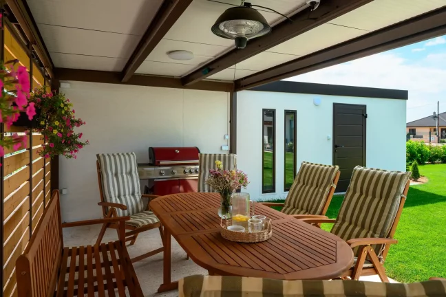 Überdachung mit rotem Grill, Tisch und Blick auf das Gartenhaus