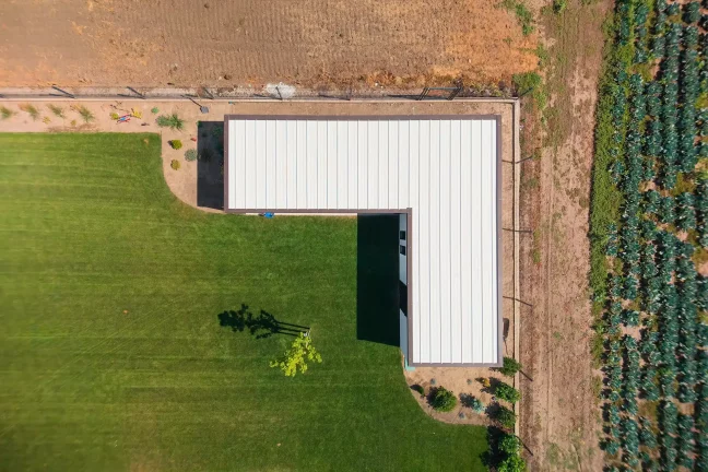 Luftaufnahme von oben mit Blick auf das weiße Dach des Gartenhauses neben einem Feld