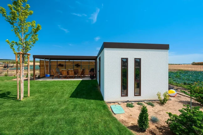 Eckansicht des weißen Gartenhauses mit hohen Fenstern und jungem Baum