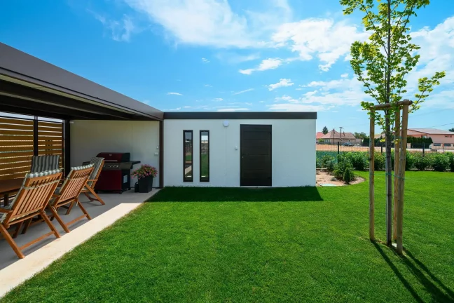 Eingangstür des Gartenhauses mit jungem Baum und Nachbarhäusern im Hintergrund