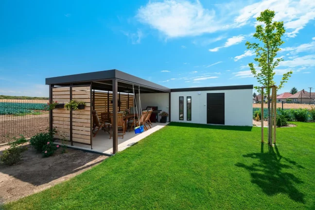 Gesamtansicht des L-förmigen Gartenhauses mit Überdachung und Garten