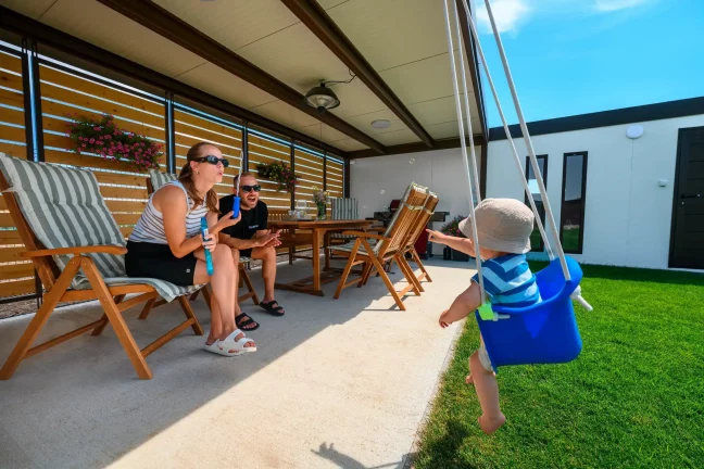 Familie mit Kind auf der Gartenschaukel vor dem Gartenhaus