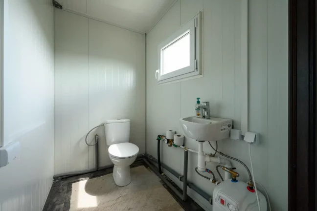 Badezimmer mit Toilette, Waschbecken und Warmwasserbereiter am Fenster