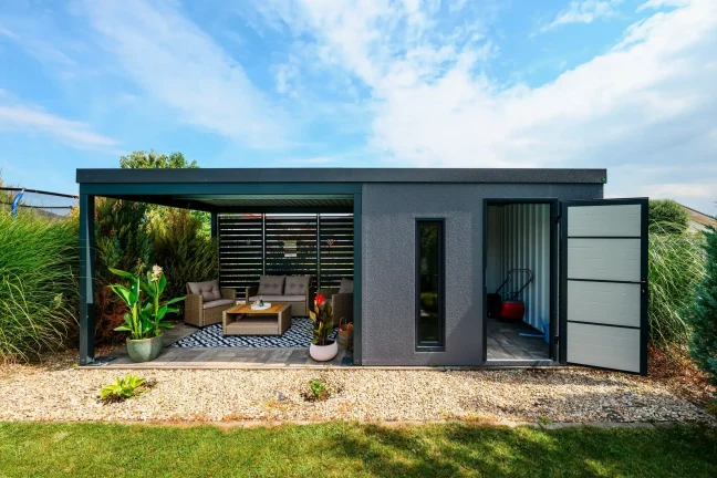 Gartenhaus mit geöffneten Türen zum Abstellraum, in dem Rasenmäher und Aufbewahrungsbox stehen
