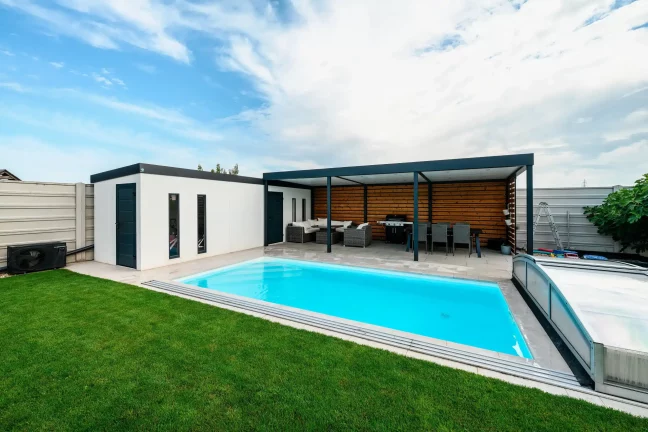 Seitenansicht des Gartenhauses, des Pools und der überdachten Terrasse mit Sofa