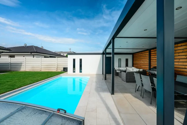 Ausblick unter der Pergola auf den Pool, das Haus und das Gartenhaus