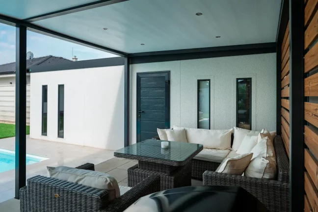 Sofa und Glastisch unter der Pergola bei den dunklen Türen