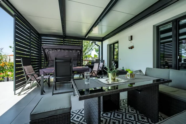 Sofa und Esstisch unter der Pergola mit Blick nach draußen