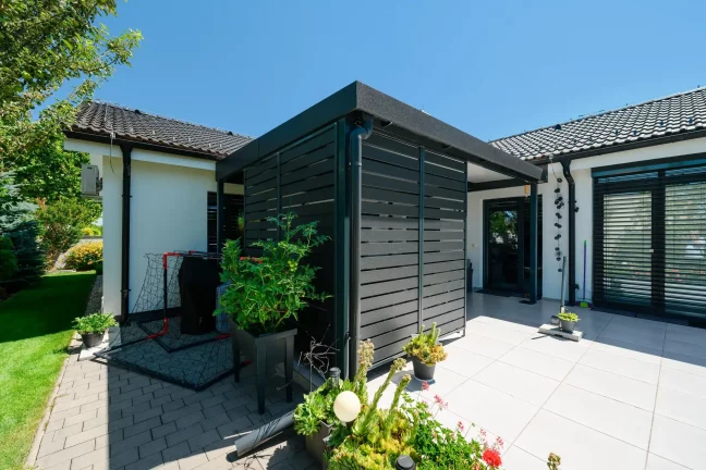 Detailansicht der Lamellenwand der Pergola mit Tomatenpflanzen und Fußballnetz