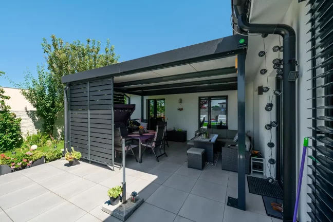 Esstisch, Schaukelstuhl und Grill unter der Pergola