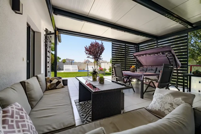 Ausblick unter der Pergola auf den Garten mit Baum und Pool