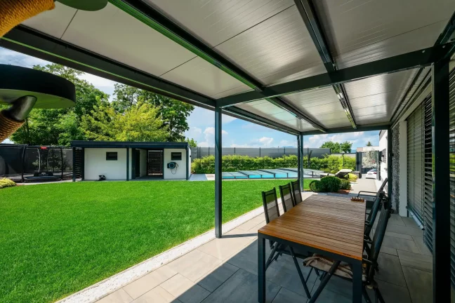 Ausblick unter der Pergola auf den Rasen, das Trampolin und den Pool