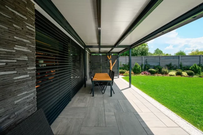 Esstisch unter der Pergola an der Steinverkleidung des Hauses