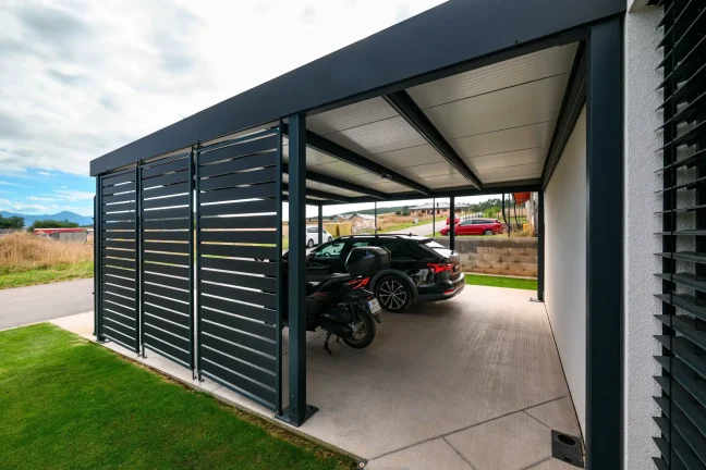 Lamellenwand des Carports mit Auto und Motorrad unter dem Dach