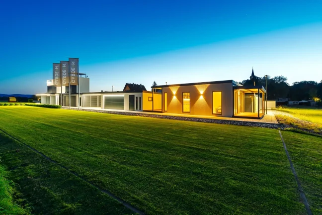 Abendansicht des beleuchteten GARDEON-Showrooms mit Tiny House