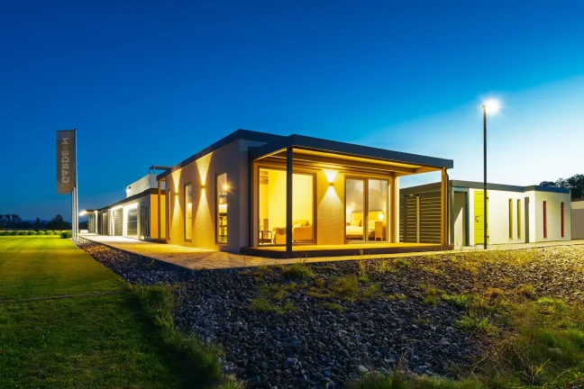 Vordere Ecke des beleuchteten Tiny Houses mit überdachter Terrasse in der Dämmerung