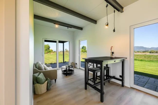 Wohnbereich des Tiny Houses mit Bartisch, Sessel und Blick durch die Glastüren